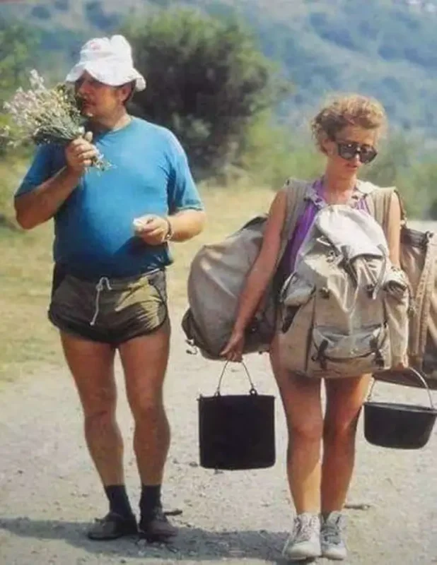 Man and teenage girl. He is holding and smelling wildfires and she is carrying camping equipment and backpacks.