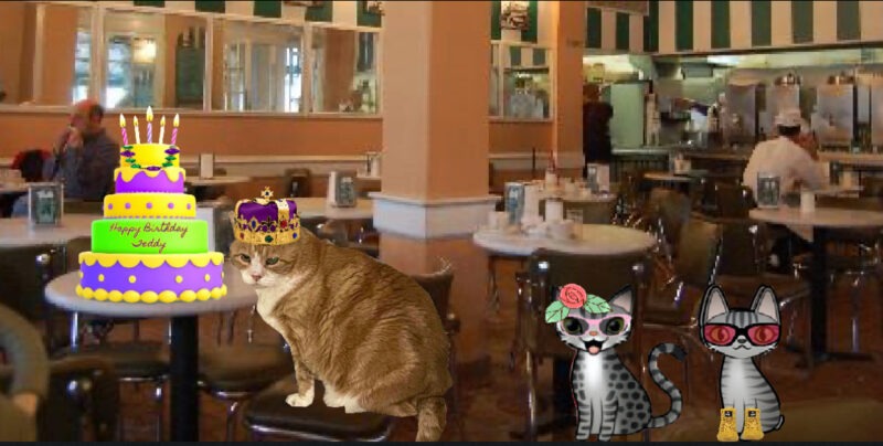 Periwinkle Stinky Mardi Gras A ginger tabby cat with a birthday cake in Mardi Gras colors with two grey cartoon tabby cats at Cafe du Monde in New Orleans.